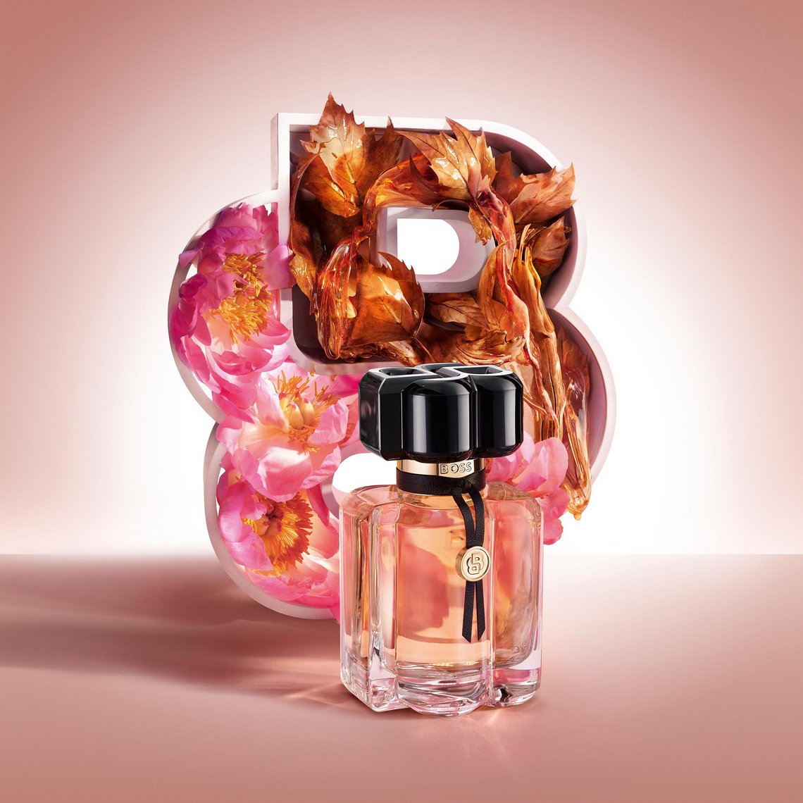 Flakon von BOSS Bottled Beyond for Her vor einem doppelten B aus rosa Pfingstrosen und goldbraunen Ahornblättern