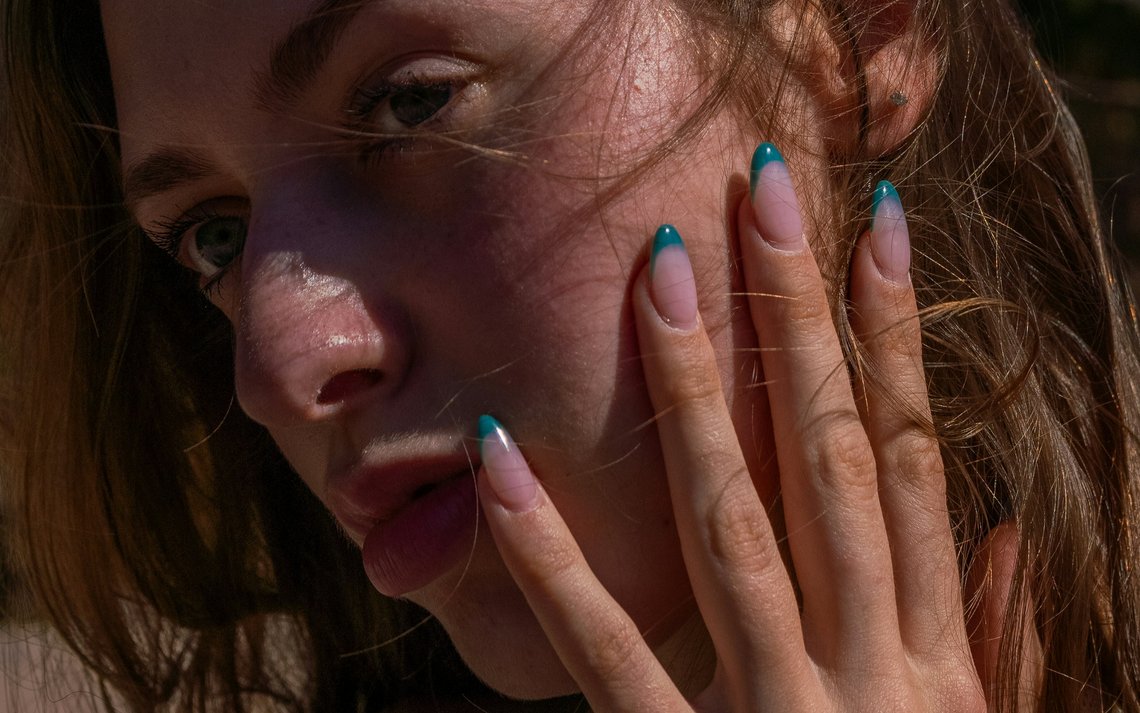 Frau mit sommerlichem French-Nageldesign in Türkis, die ihre Hand vor das Gesicht hält.