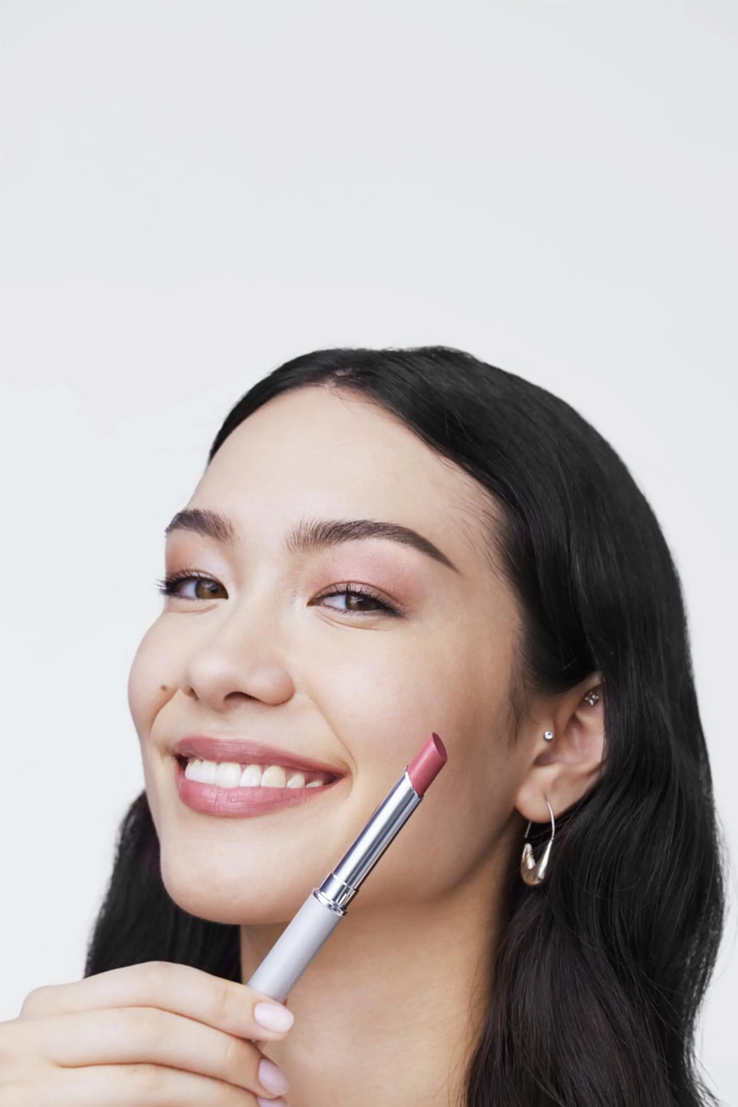 Eine junge Frau lächelt in die Kamera (Close up), hält einen Lippenstift hoch