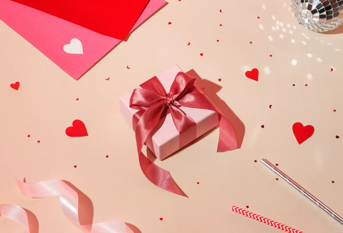 Ein rosafarbenes Geschenk mit pinker Schleife umgeben von Konfetti in Herzform