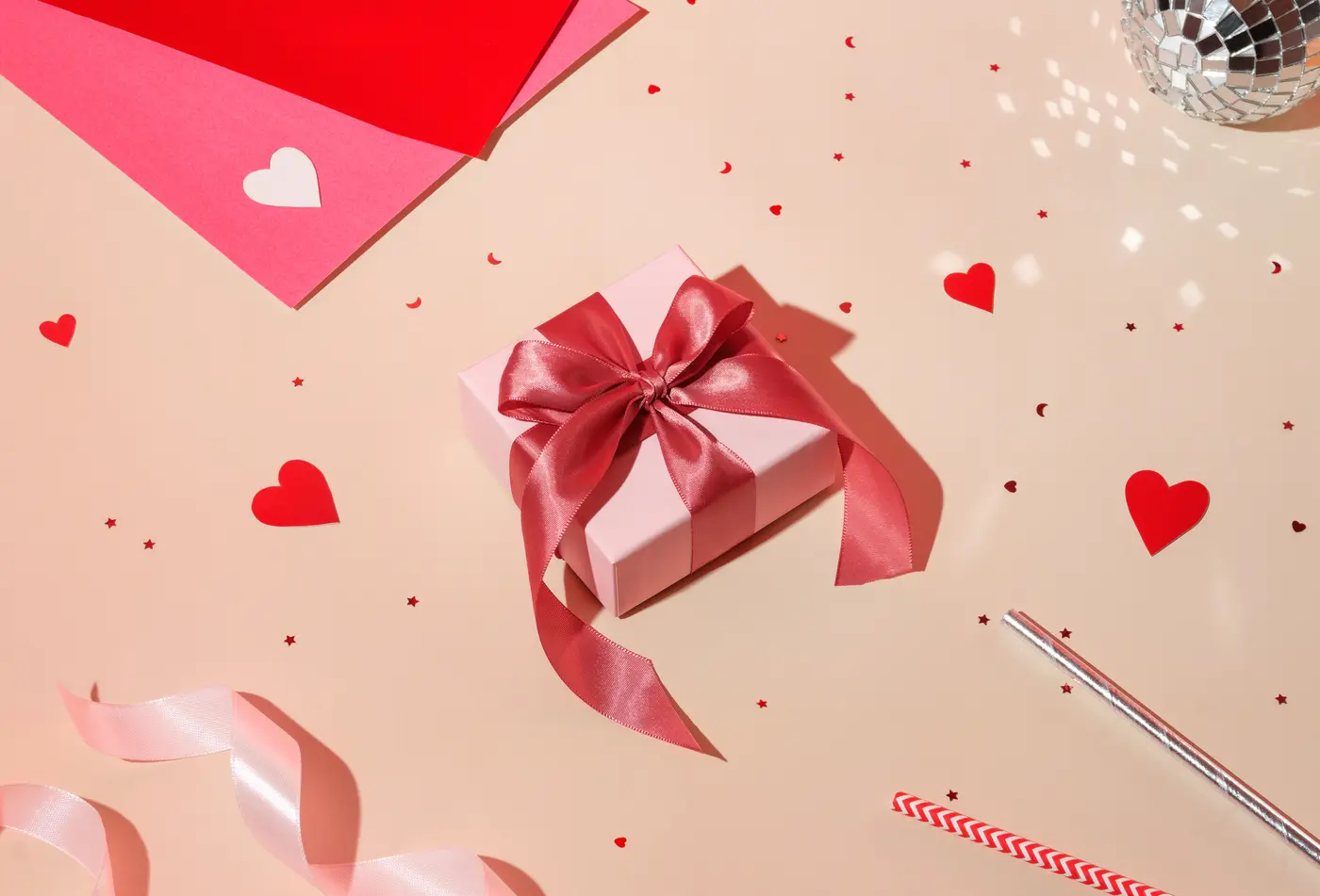 Ein rosafarbenes Geschenk mit pinker Schleife umgeben von Konfetti in Herzform