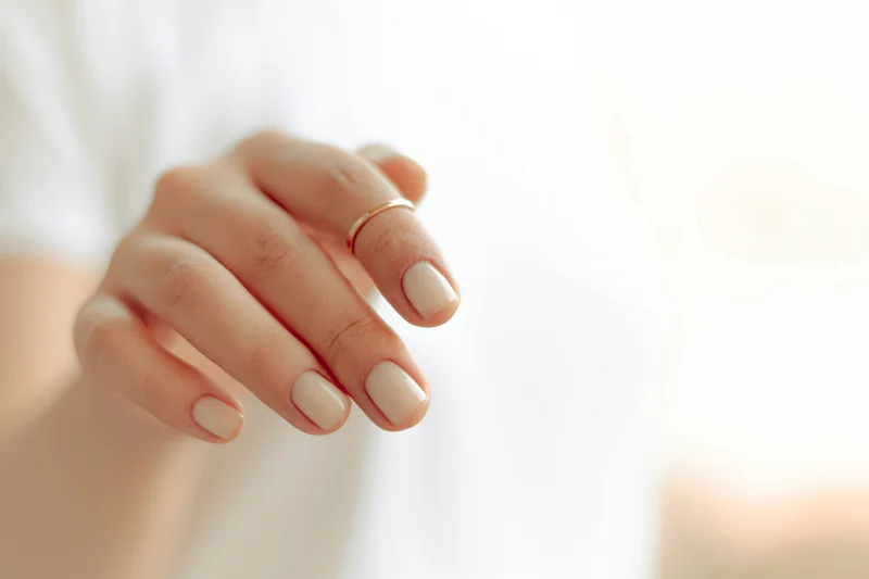 Kurze Gelnägel in einem cremigen Nude-Ton an einer Hand mit schmalem Goldring