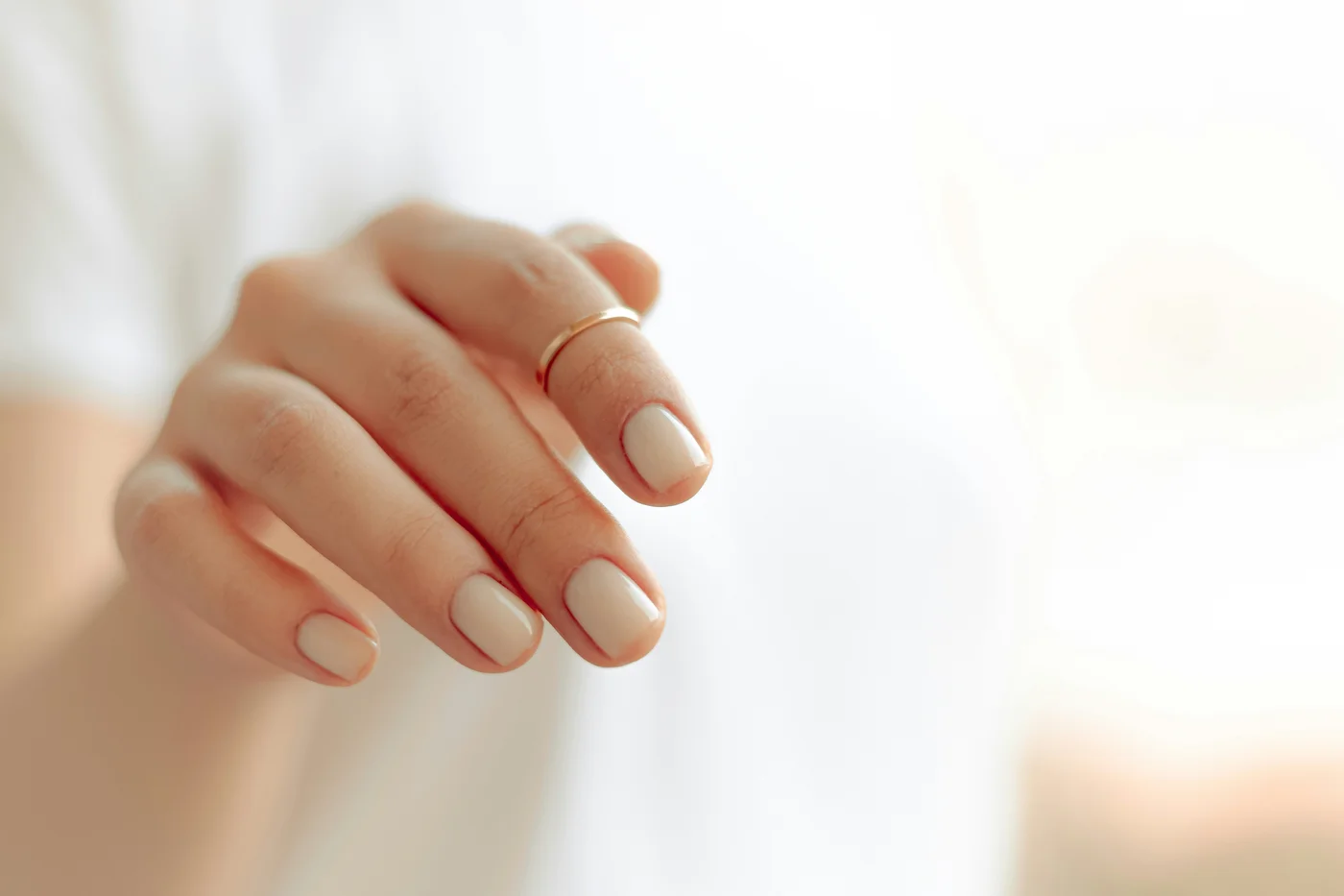 Kurze Gelnägel in einem cremigen Nude-Ton an einer Hand mit schmalem Goldring