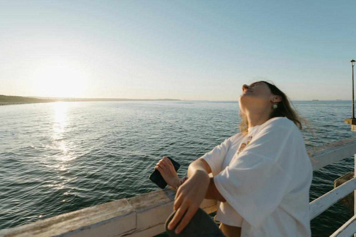 Frau hält ihr eingecremtes Gesicht am Meer in die Sonne