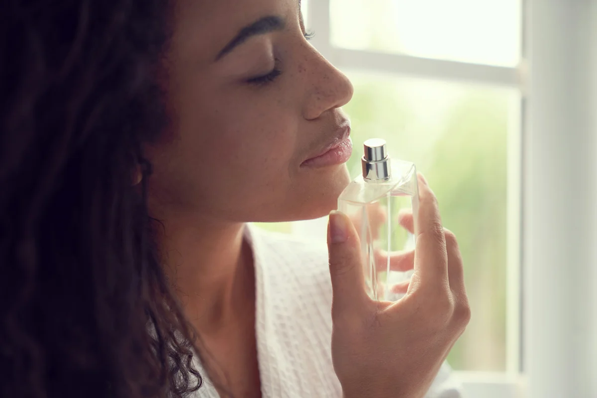 Nahaufnahme einer Frau mit lockigem Haar, die an einem Parfumflakon riecht