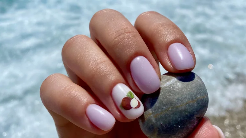 Hand mit sommerlichem Nageldesign in zartem Lavendelton und Ocean-Nailart vor dem Meer.