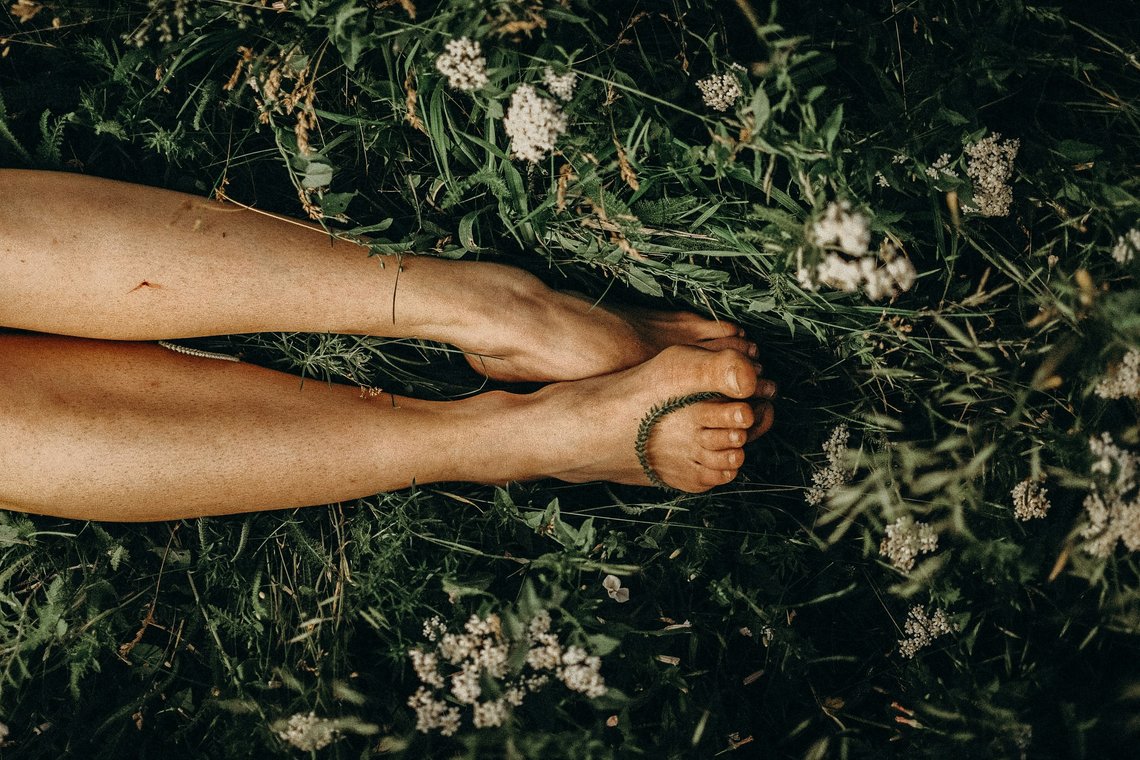 Nackte Beine einer Frau liegen entspannt in einer grünen Wiese mit weißen Wildblumen.