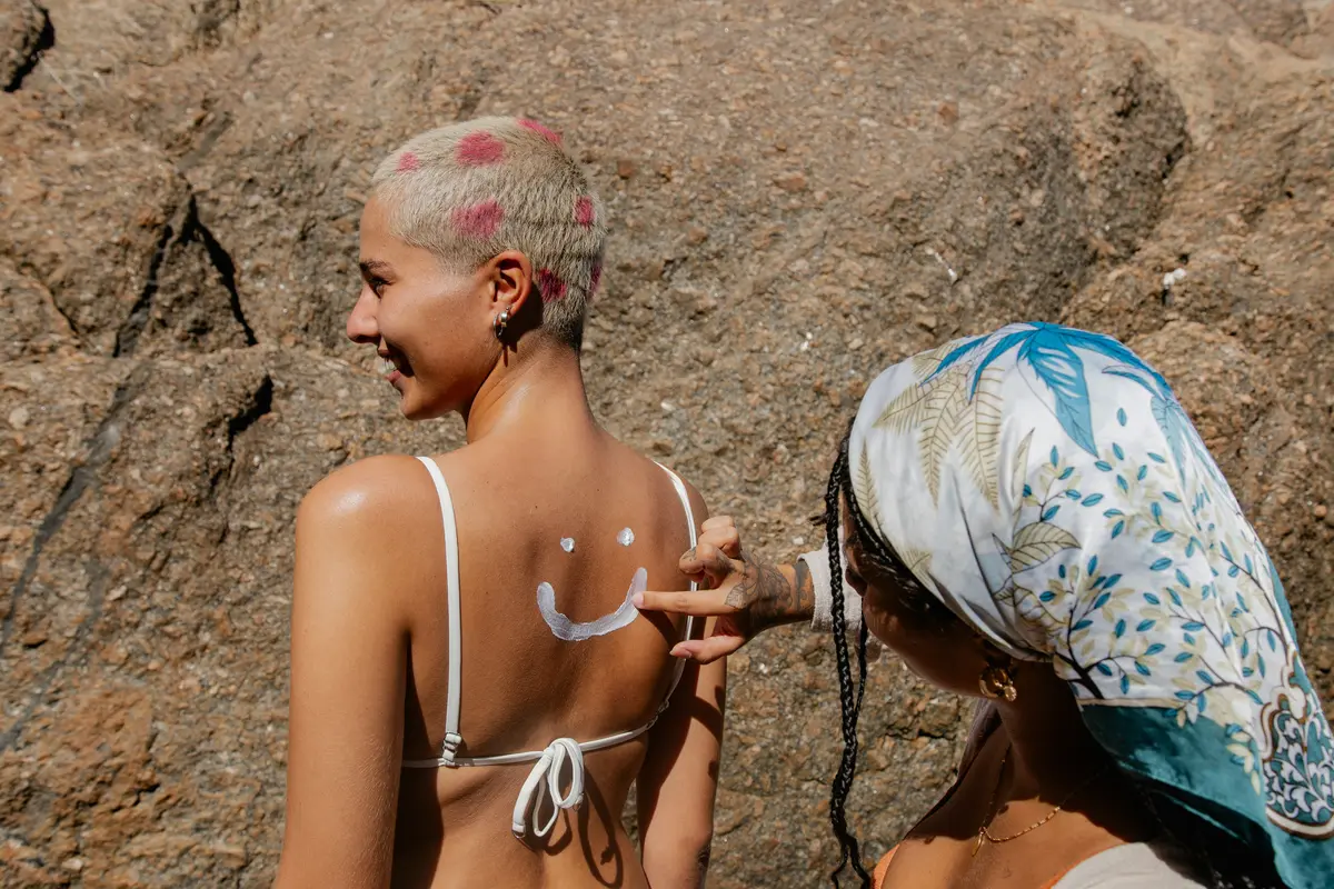Rückansicht junge Frau im Bikini, eine andere trägt Sonnencreme auf ihren Rücken