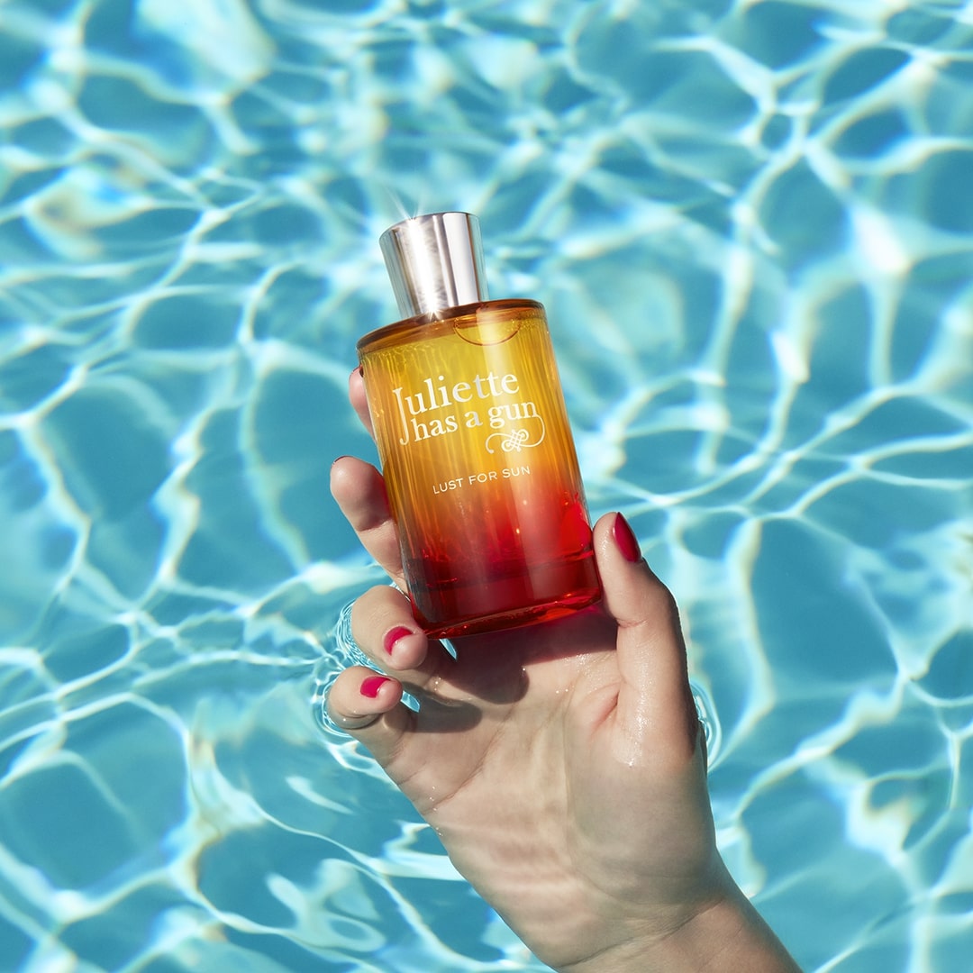 Hand hält Flakon von LUST FOR SUN in Poolkulisse, Detailaufnahme