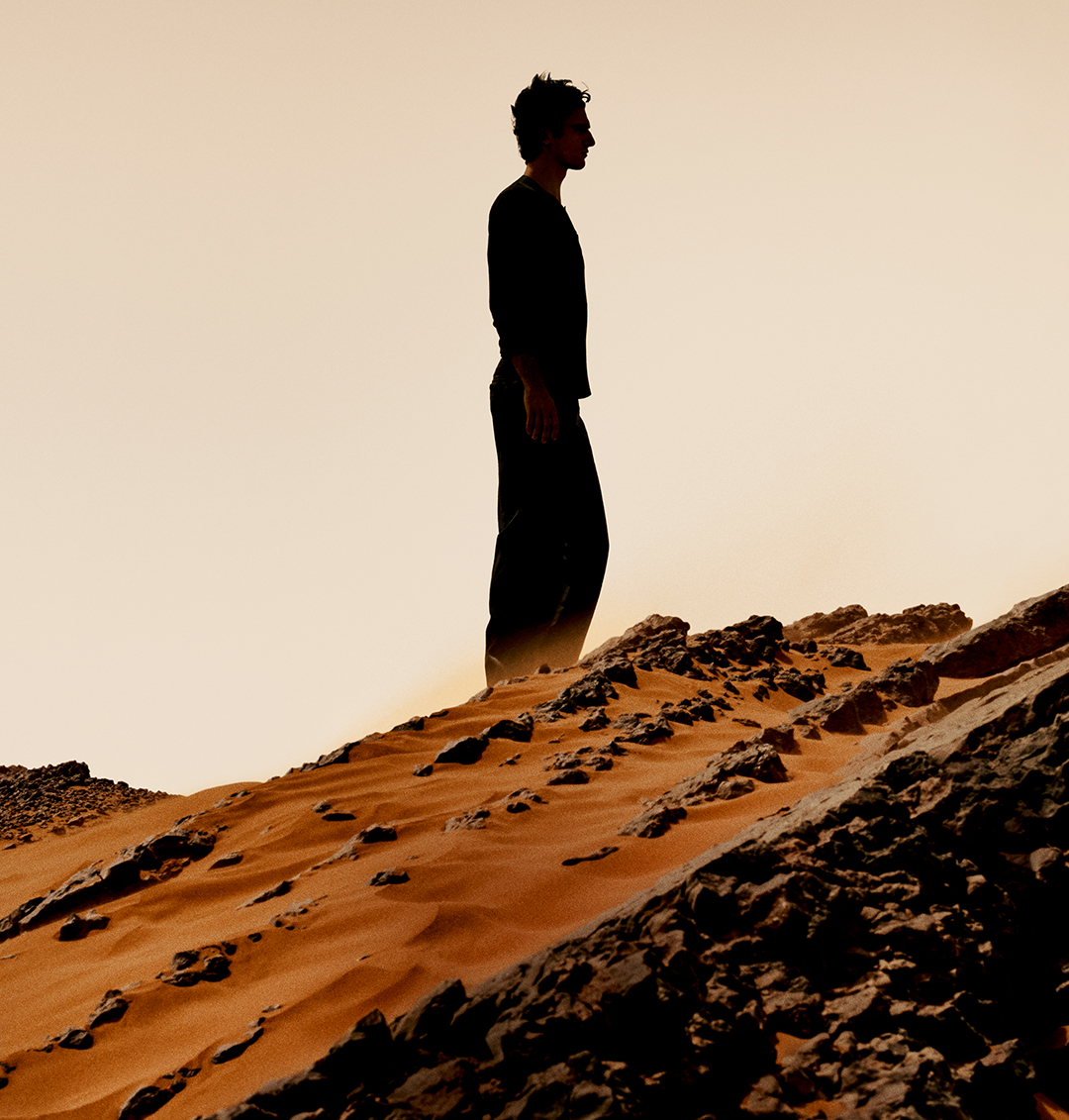 Junger Mann auf einem Sandhügel in der Wüste