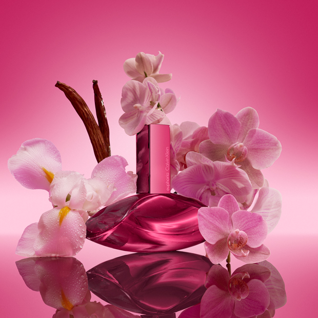 Calvin Klein Euphoria Elixir Duft in pinkem Flakon, umgeben von rosa Orchideen auf spiegelnder Oberfläche