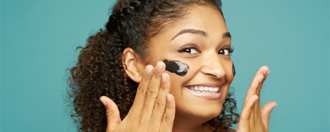 Lachende Frau trägt schwarze Gesichtsmaske auf